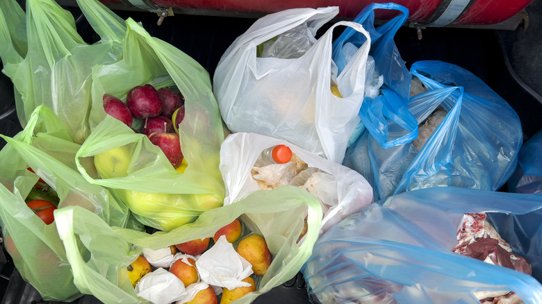Green, white, and blue plastic shopping bags are filled with groceries in a car trunk