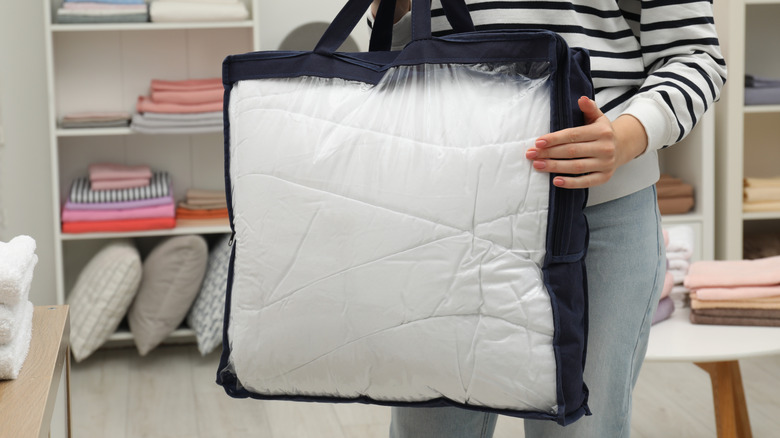 A woman holding a bedding bag with store shelves in the background.