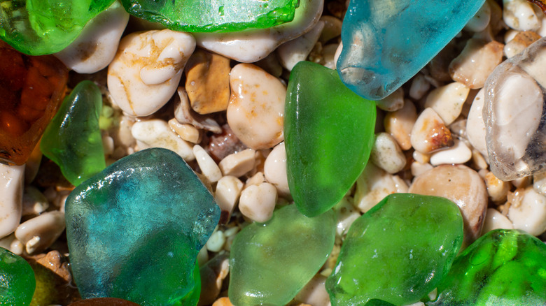 Pieces of weathered green, blue, and brown glass lie on a pebbly beach.