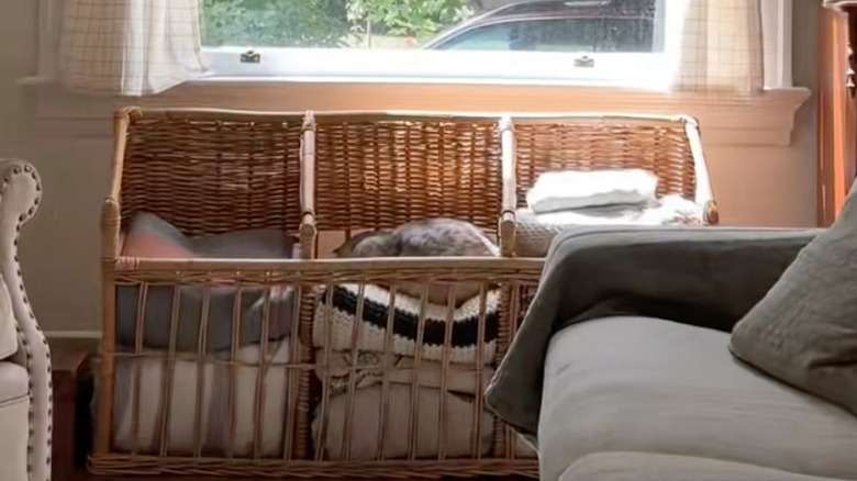 A brown vintage wicker baguette basket filled with spare blankets in a living room.