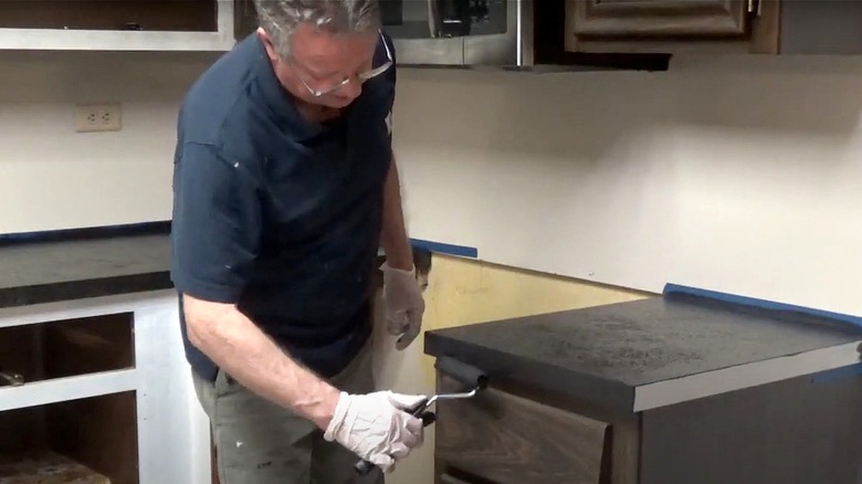 A man uses a small roller brush to resurface a kitchen countertop