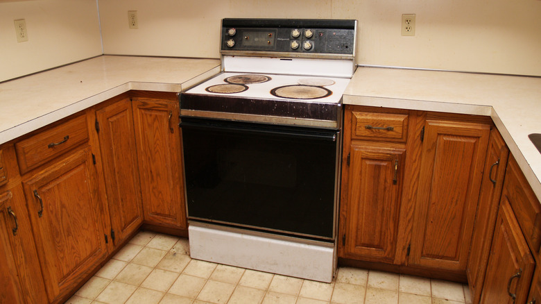 An old stove is surrounded by old laminate countertops in a dated kitchen