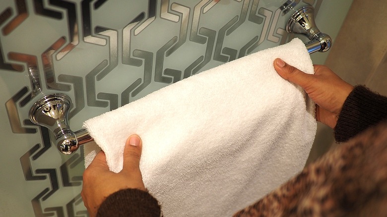 Close-up of a person hanging up a white towel on a chrome bathroom towel rack