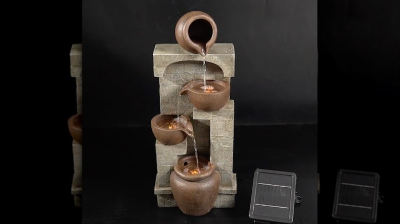 The Solar Gray Stone Wall Fountain by Teamson in a backyard in evening light slightly illuminated and running