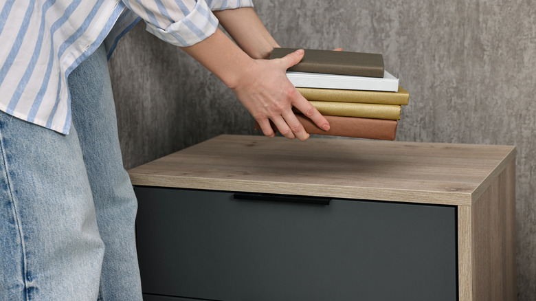 Person placing a pile of books on a nightstand