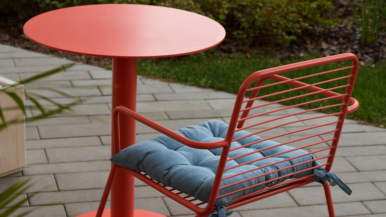 Modern red powder-coated aluminum table and chair with blue cushion on an outdoor patio.