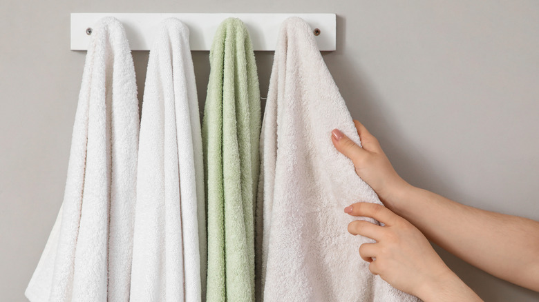 hands reaching for one of four towels hung on a wall-mounted rack