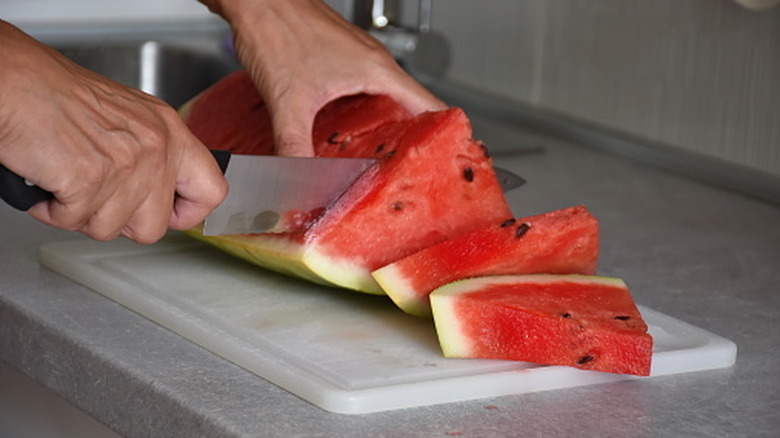 person cutting watermelon on a plastic cutting board