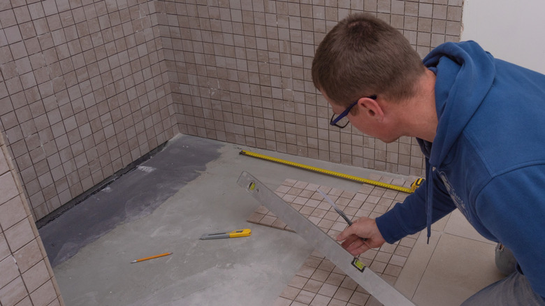 A contractor installs small square tiles in a bathroom shower