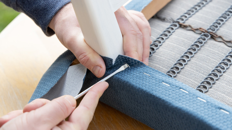A person pulling out staples on the bottom of a chair.
