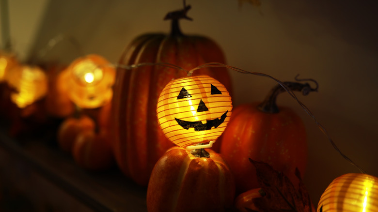 A close up of one glowing jack-o'-lantern light, part of of a set of string lights on display with decorative pumpkins.