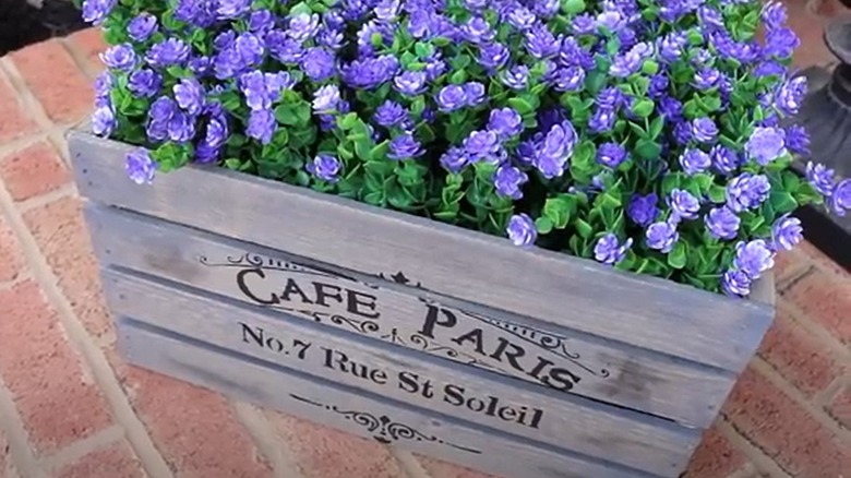 This wooden crate is painted, stenciled, and filled with flowers for a porch decor piece.