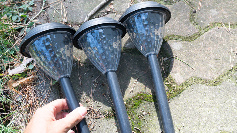 Person picking up one of a trio of solar garden lights lying on flagstone