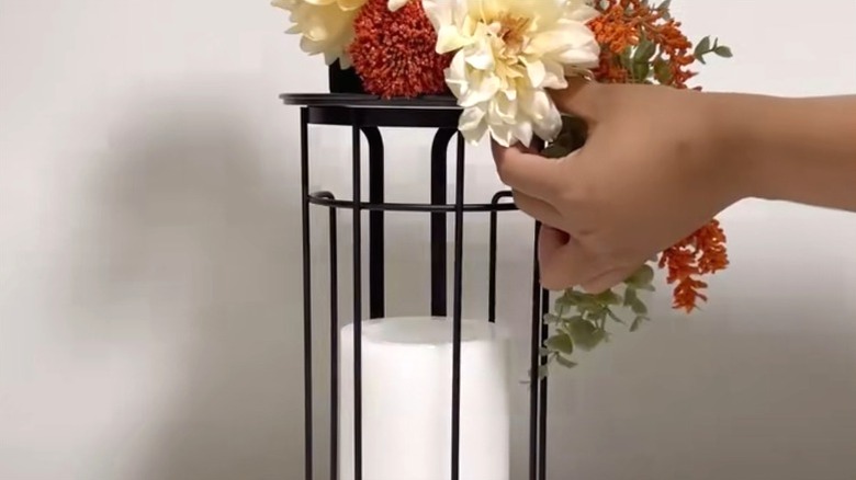 person assembling floral arrangement atop a candleholder made from a repurposed toilet paper holder