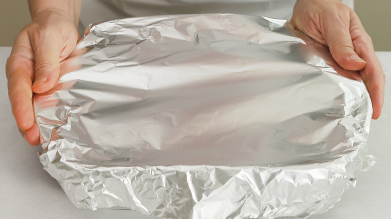 hands wrapping container in foil