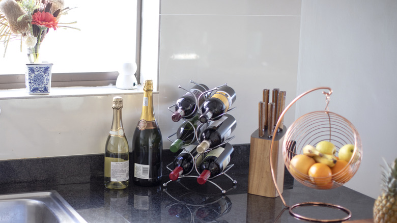 Wine bottles, a knife block, and a fruit hammock on a kitchen counter.