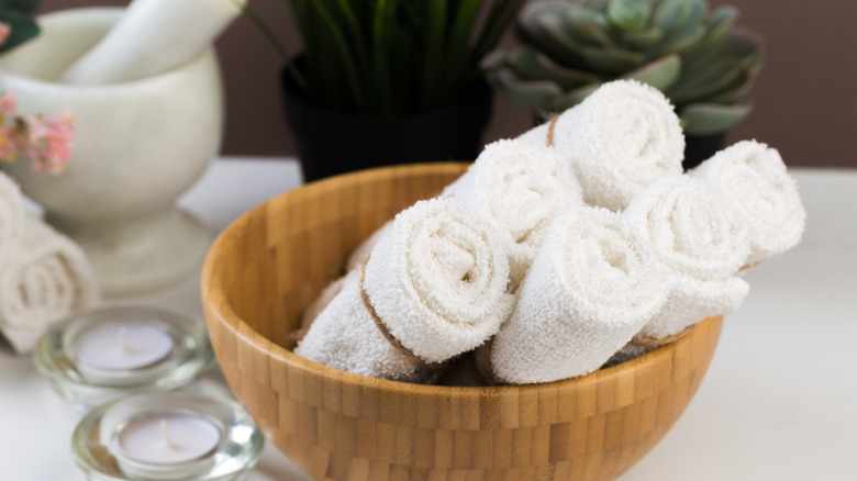 Six rolled hand towels sitting in a wooden bowl