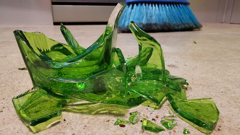 A blue broom sweeps up shards of green glass.