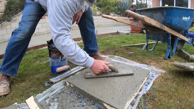 A person bending at the waist to smooth wet concrete with a trowel