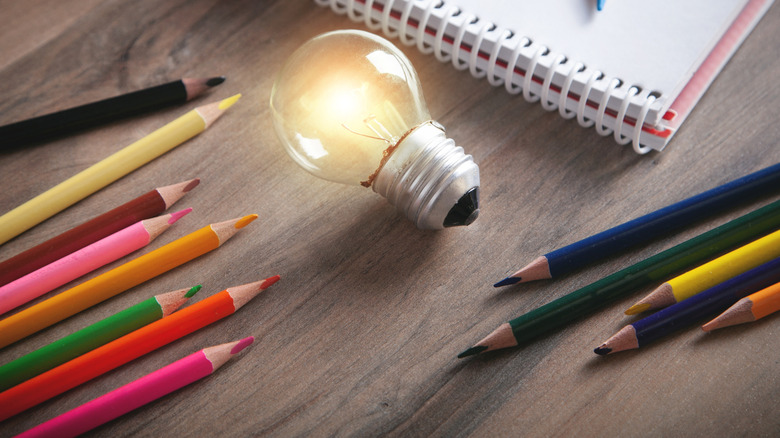 Colored pencils on a table beside a glowing light bulb