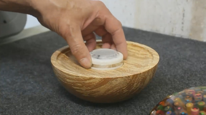 Hand inserting a puck light into wood DIY lamp base