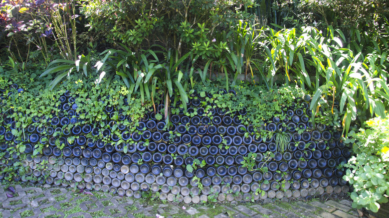 A short retaining wall made from blue glass bottles holds a flower garden.