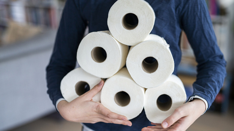 person holding a tower of toilet rolls