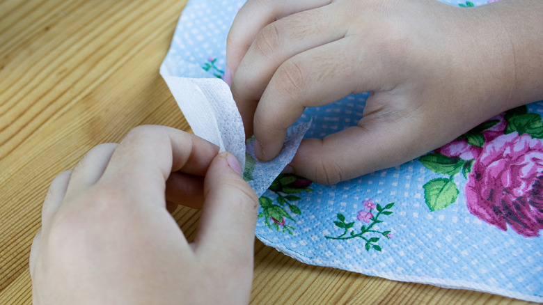 Two hands pull apart floral tissue for decoupage.