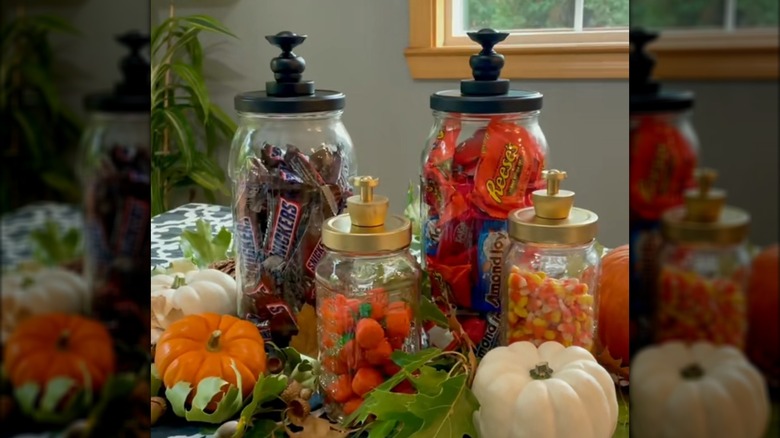 Glass jars made from pickle jars holding candy and surrounded by pumpkins, leaves, and other fall decor
