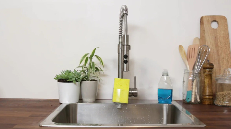 A plastic bottle top transformed into a hanging sponge holder on a sink.