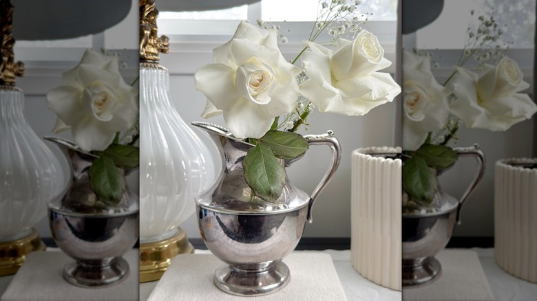 Vinatage silver creamer pitcher used as a nightstand flower vase with white roses.
