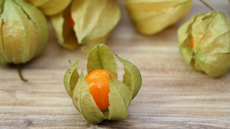 Ripe ground cherries with husks peeling away sit on a wooden counter.