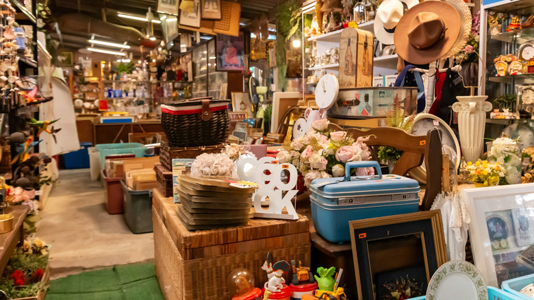 Cluttered thrift shop with an assortment of home goods, chairs, framed art, and decor