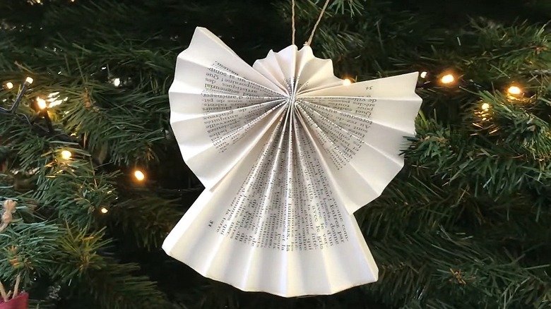 Paper angel ornament made from book pages hanging on a tree with white lights