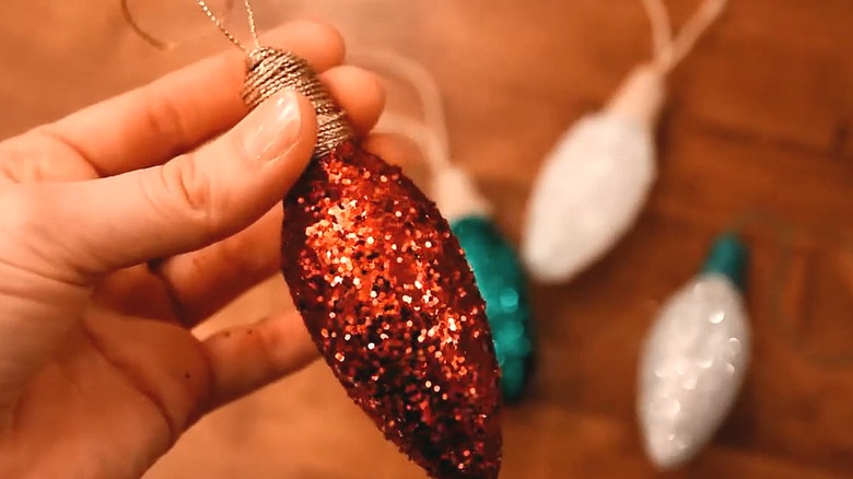 Person holding a red glitter-covered bulb ornament with other colors in the background