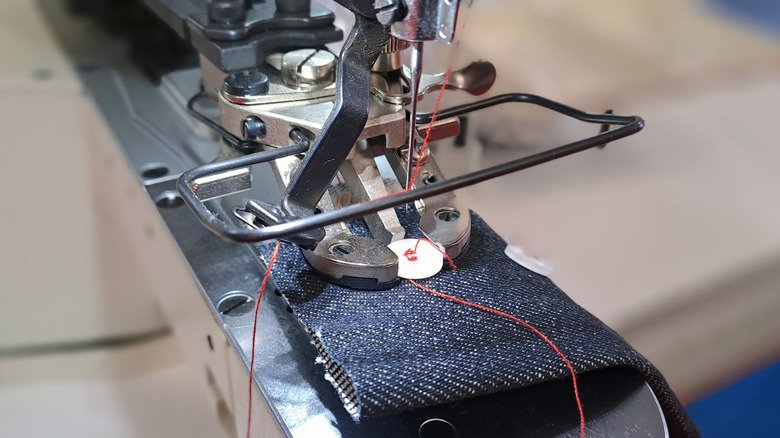 A close up of a sewing machine using red thread to sew a piece of dark blue denim