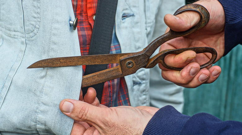 A person cutting light blue denim with large rusty scissors
