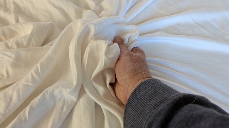 A light skinned hand rumples white bamboo sheets.