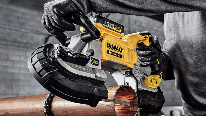 A person using a DeWalt band saw to cut through a metal pipe.