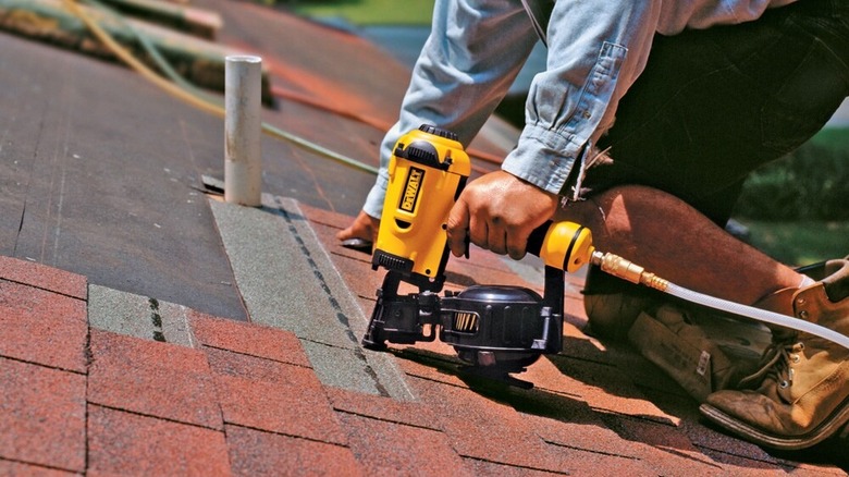 A person holding a DeWalt roofing nailer to a roof.