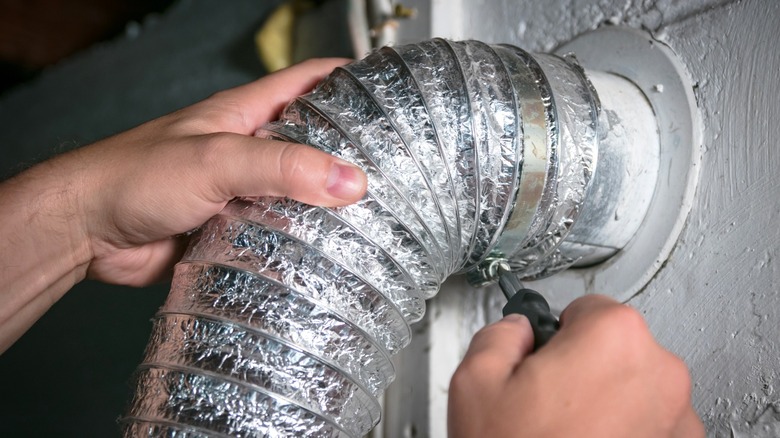 Person loosening dryer vent tube clamp connected to wall port