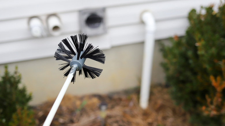Dryer vent cleaning brush outside with dryer vent exhaust in background