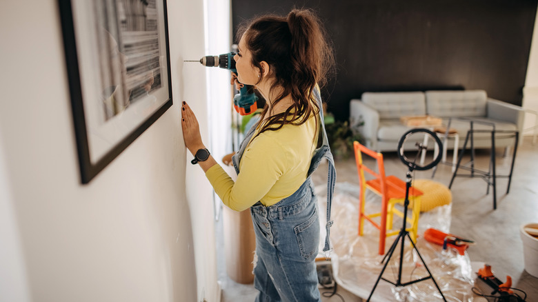 Young woman drilling a hold in the wall to hang a picture