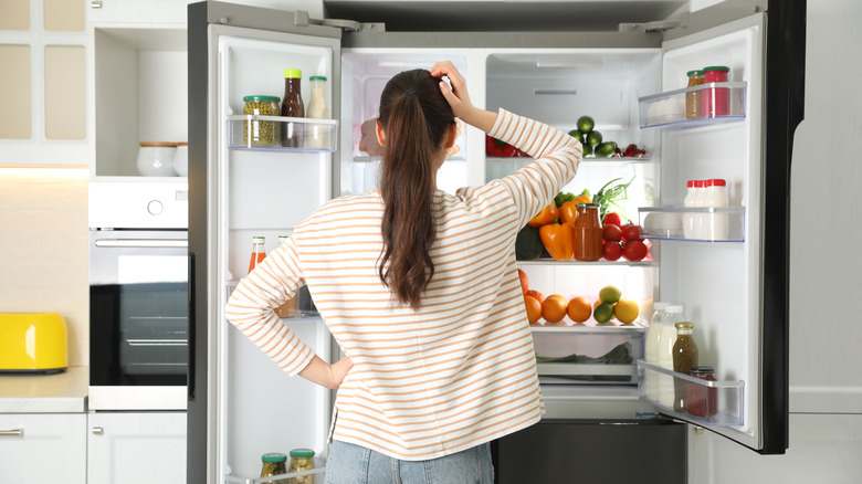 woman looking in disorganized fridge