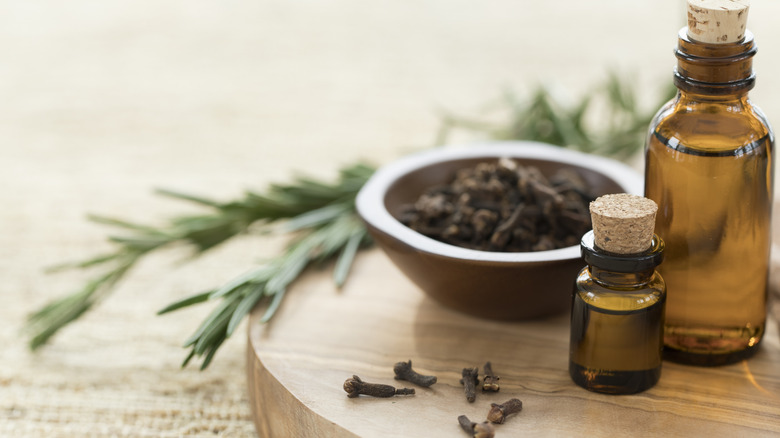 Rosemary and cloves sit next to bottles of essential oil on a wooden tray.