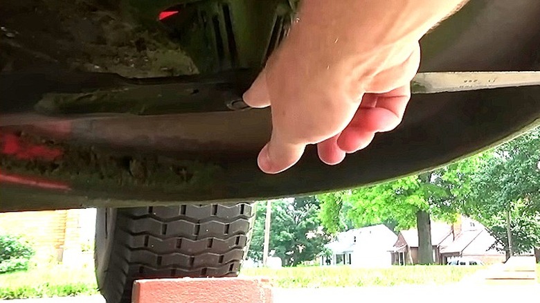 Close-up of a person's hand reaching for the blade beneath a riding lawn mower