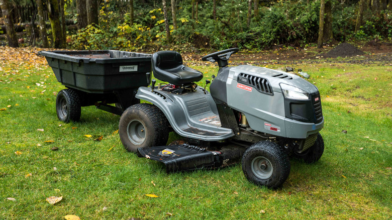 A Craftsman riding lawn mower on a lawn with a dump cart attached behind it.