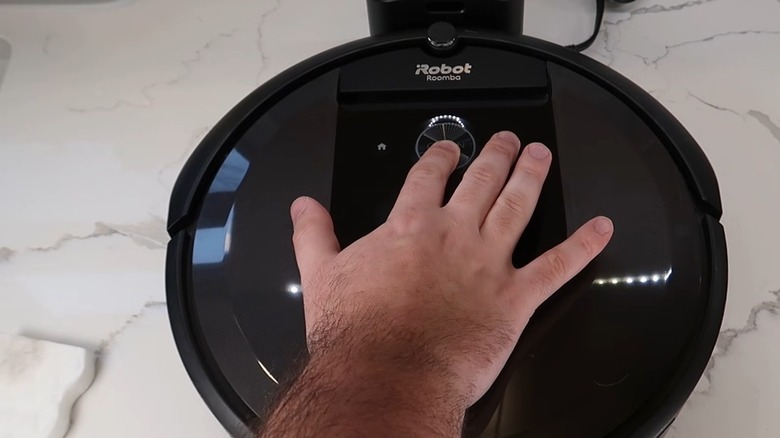 Finger pressing the POWER button on a black Roomba
