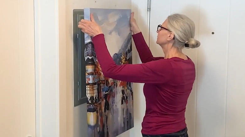 Woman hanging a painting over an electrical panel