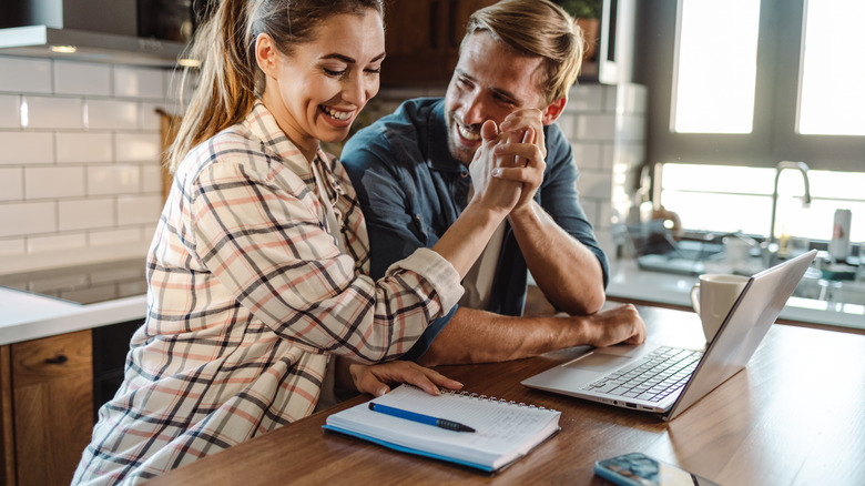Couple high-fiving at laptop in kitchen